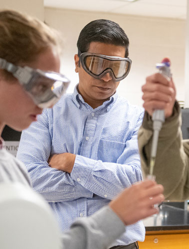 A faculty member supervising two students in a chemistry lab.