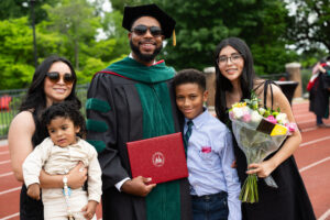 RS65484_20240517-4419 DMSc graduate standing with family and holding diploma